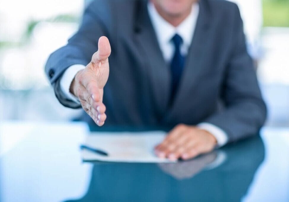 Businessperson reaches across desk to shake hands