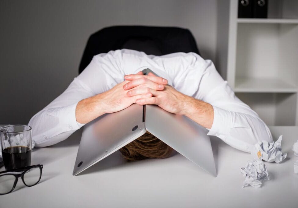 Man with head on desk covered by his laptop